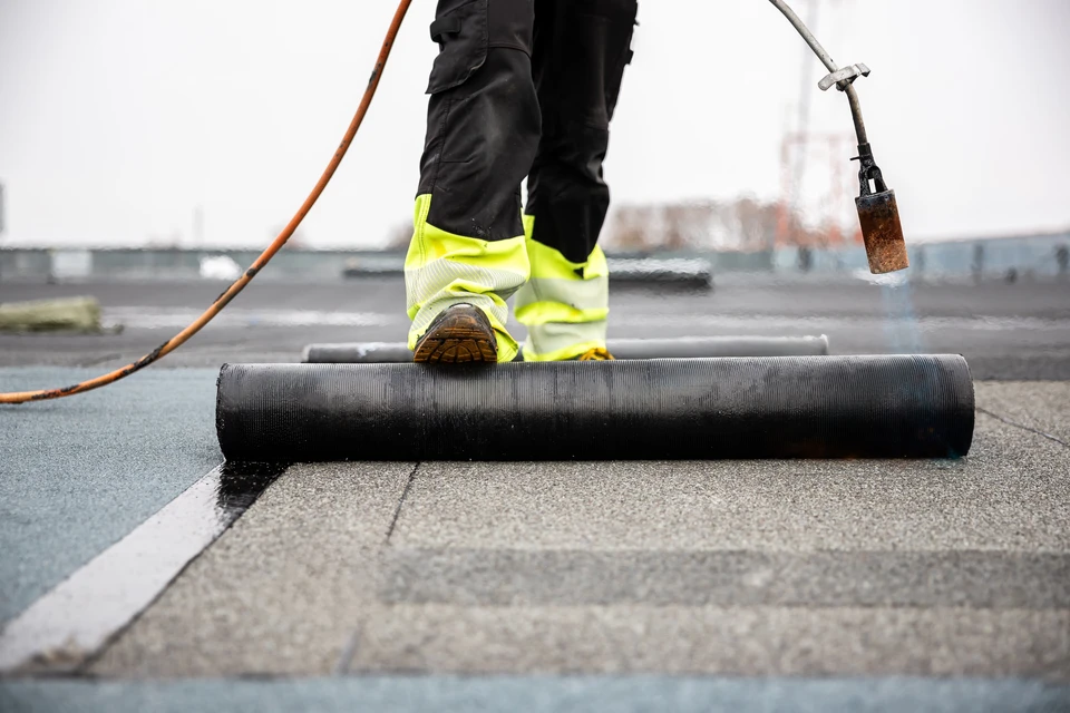 toit professionnel appliquant du goudron avec une lampe à torche sur un nouveau feutre pour l'imperméabilisation d'un chantier de construction à toit plat avec équipement de sécurité