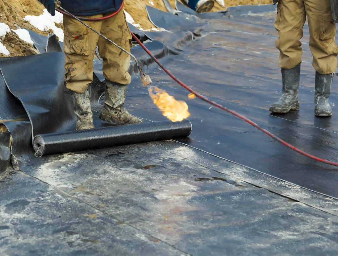 Chantier extérieur d'étanchéité avec ouvriers en combinaisons de protection appliquant membrane bitumineuse au chalumeau