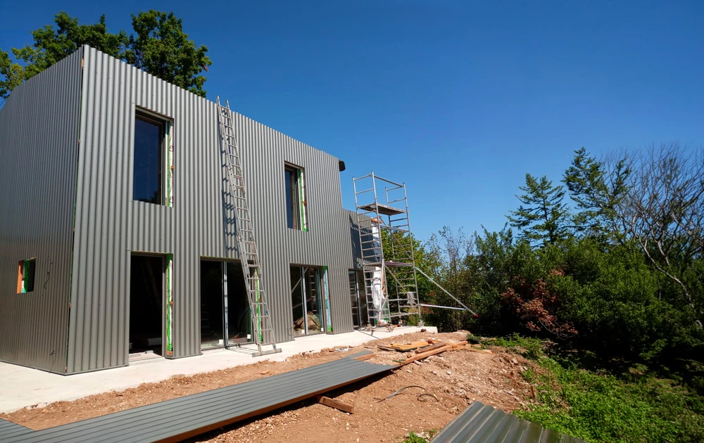Maison moderne en cours de construction, vue extérieure, bardage métallique vertical gris anthracite, style cubique contemporain