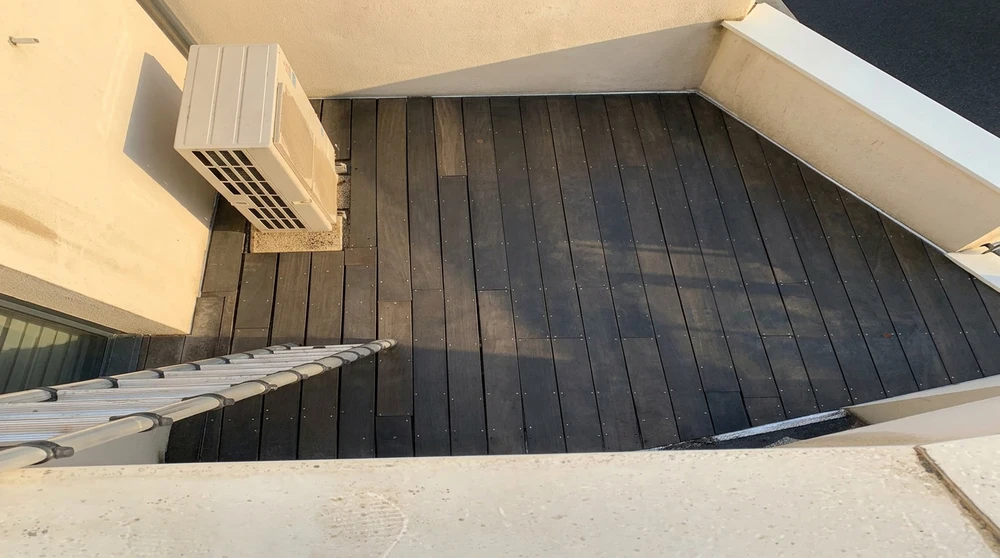 Terrasse extérieure vue en plongée, revêtement de lames composites dark/charbon posées horizontalement, fixation par vis apparentes